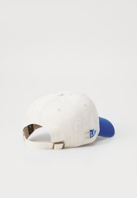 Căciulă de baseball cu un corp din bumbac alb și vizieră albastră, curea ajustabilă la spate și o brodare logo în albastru și gri.