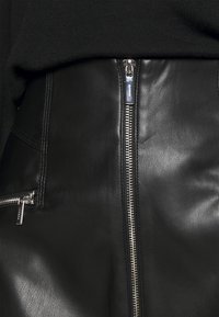 Falda de cuero negra con una cremallera metálica visible, que presenta bolsillos laterales y un acabado liso y texturizado. Incluye detalles de costura a lo largo de los bordes.