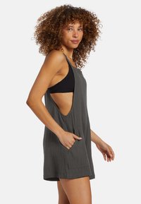 Vestito grigio senza maniche, con una vestibilità ampia, aperture laterali e tasche frontali. Realizzato in tessuto leggero, con una superficie testurizzata.