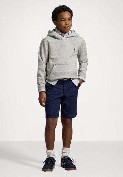Grå hettegenser med frontlomme, marineblå shorts, kremfargede sokker og mørke joggesko. Uformell antrekk med lagdelte designelementer.