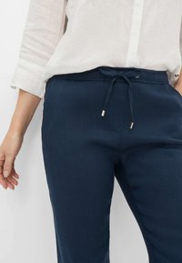 Pantaloni leggeri blu navy con elastico in vita, dotati di aghetti metallici e un tessuto liscio e testurizzato. Design slim fit.