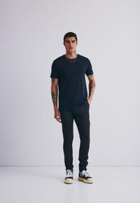 Černé tričko spárované s úzkými tmavými kalhotami. Model má na sobě bílé a černé tenisky. Jednoduchý design, krátké rukávy a kulatý výstřih.