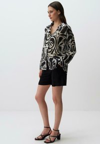 Blusa a righe in bianco e nero con maniche lunghe, colletto e tasche, abbinata a pantaloni corti neri e sandali con tacco a blocco e fasce.