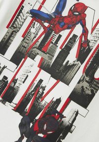 T-shirt blanc avec des graphismes rouges et noirs de Spider-Man au milieu d'un design de skyline urbain, présentant une pose d'action dynamique et un art de style bande dessinée.