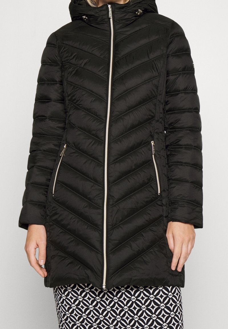 Schwarze Steppjacke mit Zickzacksteppung, Reißverschluss vorne und Kapuze. Mit goldenen Reißverschlüssen und Seitentaschen. Leichtes synthetisches Material.