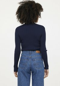 Marineblauer, gerippter Pullover mit langen Ärmeln, kombiniert mit hoch taillierten, hellblauen Jeans aus Denim, die zwei Gesäßtaschen und ein Lederlabel am Bund haben.