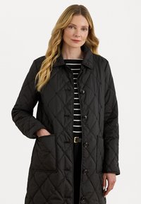 Zwarte gewatteerde coat met knoopsluiting, kraag en twee zijzakken, met een gestructureerd ruitpatroon en lange mouwen.