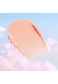 Smooth, peach-colored cosmetic cream swatch against a soft blue sky with pink clouds background.