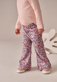 Uppflådiga byxor med blommigt mönster i rosa, lila och röda nyanser, gjorda av mjukt tyg. Kombinerade med ljusfärgade skor.