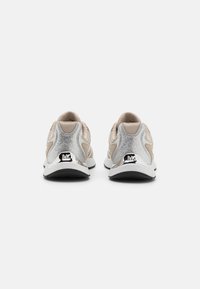 Lette joggesko med en beige og sølvfarge, som har en teksturert overflate, logo-oppmerkinger, og en dempet såle for komfort.
