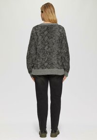 Grijze gebreide trui met een zachte textuur, wijde mouwen en een contrasterende grijze zoom, gecombineerd met zwarte broek en donkere schoenen.