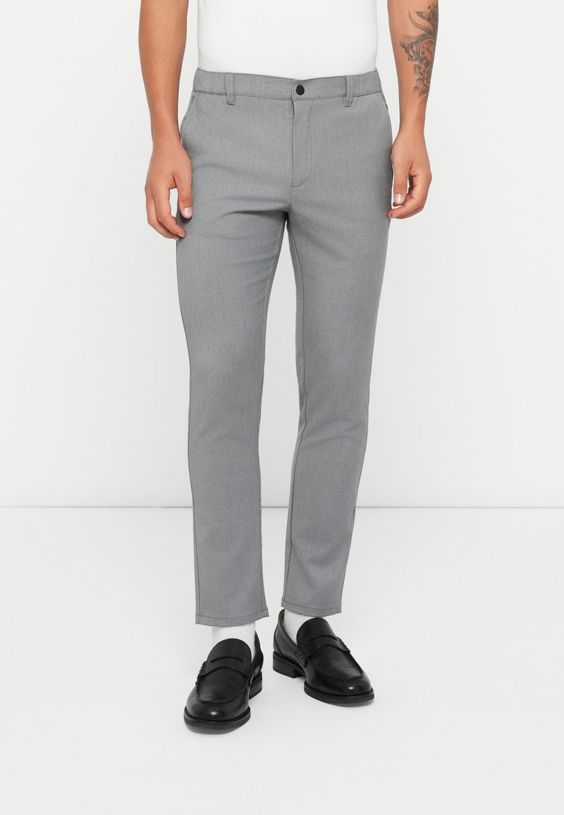 Pantalones grises a medida con un acabado de tela suave, diseño ajustado, bolsillos delanteros y cierre de un solo botón. Se llevan con mocasines negros.