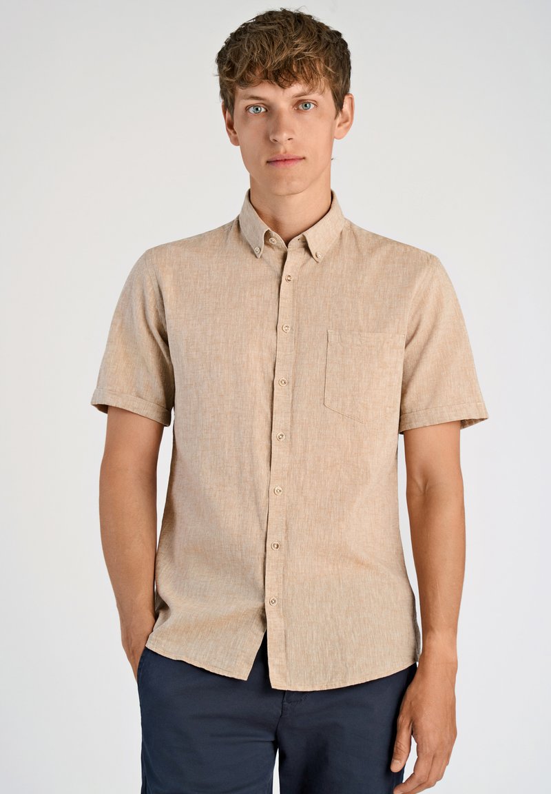 Camicia corta con maniche corte di colore beige, con colletto a punta e taschino. Tessuto morbido e testurizzato, con un leggero motivo mélange e bottoni in madreperla.