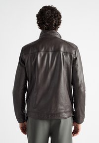 Bruine leren jas met een gladde textuur, voorzien van een hoge kraag en naaddetails. Het ontwerp aan de achterkant is eenvoudig en op maat gemaakt.