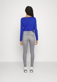 Jeans grises ajustados con bolsillos traseros, combinados con una blusa de manga larga azul brillante. El conjunto se completa con zapatillas blancas.