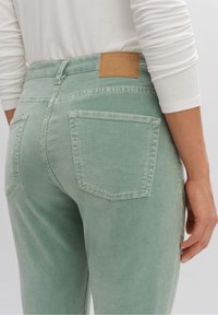 Jeans verde claro con una textura suave, que cuentan con dos bolsillos traseros y una etiqueta de cuero marrón en la cintura.