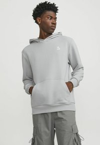 Grå hoodie med kenguruficka, ribbade ärmslut och snörad huva; har en liten vit logotyp på bröstet och bärs med grå cargobyxor.