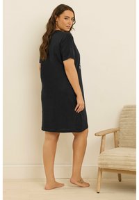 Czarna bawełniana sukienka t-shirt z krótkimi rękawami, luźny krój, sięgająca do połowy uda. Prosty wzór, miękka tekstura, gładka powierzchnia, brak widocznych wzorów.