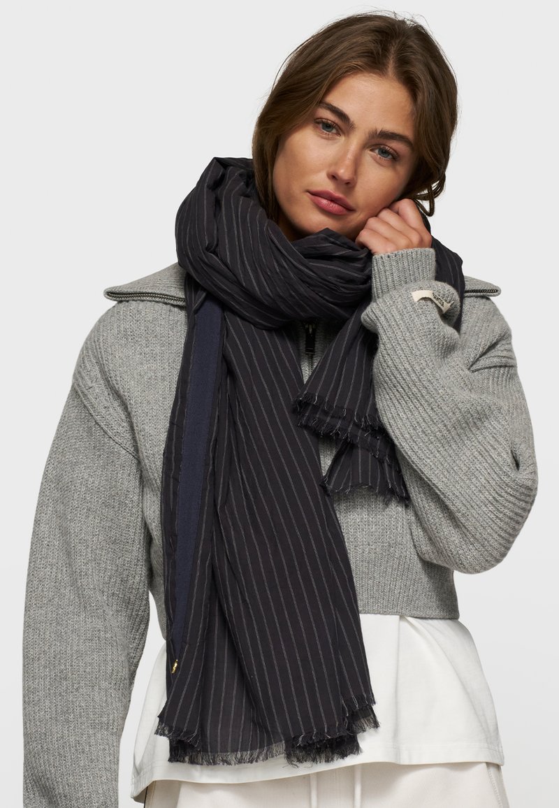 Écharpe rayée noire en tissu doux, avec des bords effilochés et un mélange de motifs unis et à rayures fines pour une texture ajoutée.