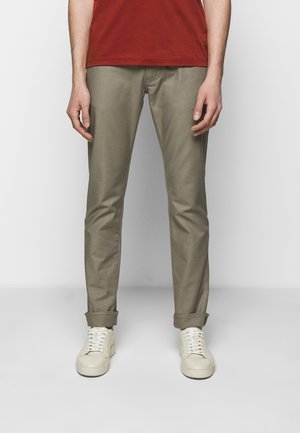 Khaki chinot, joissa on slim fit ja käännetyt hihanapit, valmistettu sileästä kankaasta. Yhdistettynä kermaisiin lenkkareihin ja punaiseen t-paitaan.
