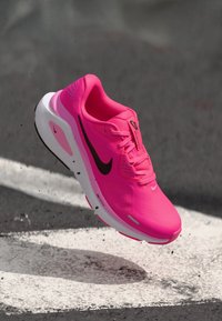 Neon-pinke Sportschuh mit einem strukturierten synthetischen Obermaterial, weißer Zwischensohle und schwarzem Swoosh-Logo; ausgestattet mit Schnürung und atmungsaktiven Mesh-Details.