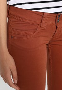 Ruskvärgade byxor med smal passform, tillverkade av bomullsblandning. Har två knappar, framfickor och sydda detaljer på fickorna.