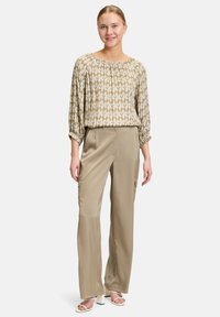 Blusa beige con motivo e scollatura arricciata, abbinata a pantaloni a gamba larga color khaki chiaro. Tessuto morbido con leggera lucentezza e maniche con polsino.