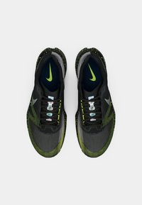 O pereche de pantofi de alergare Nike negri cu verde neon văzuți de sus pe un fundal alb simplu.