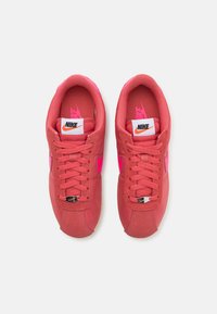 Rózsaszín Nike sportcipők hálós és velúr felsőrésszel, lapos fűzőkkel, kontrasztos rózsaszín pipa logóval, valamint fehér emblémával a nyelven. Gumitalp.