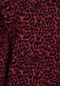 Burgundiškai raštuota leopardų spauda, kuriame yra juodų dėmių ant tekstūruoto audinio. Vienoje pusėje yra raukiniai. Bendras paviršius lygus.