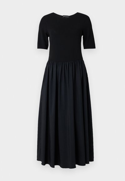 Čierne šaty s priliehavým vrchom s krátkymi rukávmi a splývavou nariasenou sukňou. Vyrobené z jemnej tkaniny, majú okrúhly výstrih.