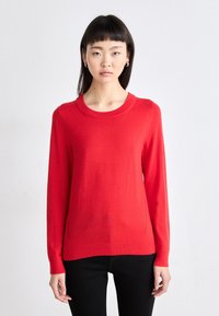 Κόκκινο πλεκτό πουλόβερ με μακριά μανίκια, στρογγυλή λαιμόκοψη και απαλή υφή. Στενή γραμμή με ριμπ μανσέτες και στρίφωμα.