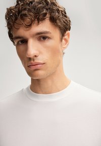 Weißes T-Shirt mit Rundhalsausschnitt aus weichem Baumwollstoff. Nahaufnahme zeigt glatte Textur und natürliche Passform am Halsbereich.