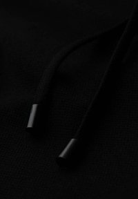 Gros plan sur les cordons d'un hoodie noir avec des embouts en plastique noir sur un fond de tissu noir texturé.