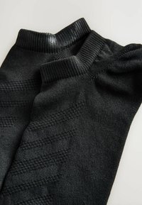 Schwarze Socken mit gerippten Bündchen und einem strukturierten Muster an den Seiten, die eine glatte Oberfläche und dezente Details im Stoff aufweisen.