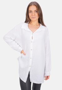 White button-up shirt in lightweight, textured fabric with a collar, long sleeves, and side pockets. Straight hem with slight curvature at the back.