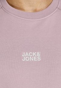 Ljusrosa sweatshirt med ribbad halsringning; har vit text "JACK&JONES" på framsidan. Mjuk tygkänsla.