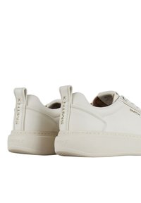 Sneakers bianchi in pelle con profilo basso, punta rotonda e accenti beige. Presentano una suola piatta e un'etichetta al tallone con logo per una vestibilità sicura.