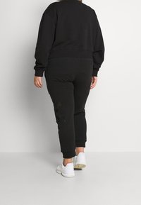 Sudadera negra y pantalones a juego, hechos de material suave. Presenta un corte relajado, puños de canalé y un detalle de logo sutil en los pantalones.