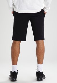 Svarta träningsshorts i bomullsblandning, knälånga, med en slät yta. Bärs med vita strumpor och svarta sneakers.