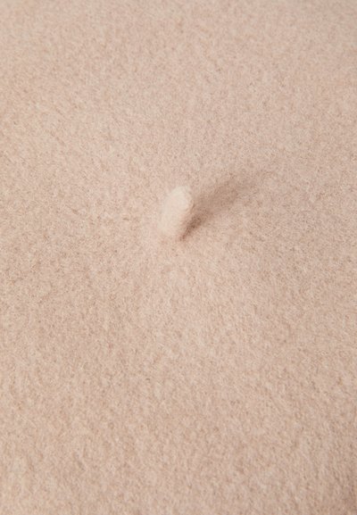 Světle růžová plstěná textilie s měkkou texturou, která má uprostřed vyčnívající detail. Povrch je hladký a mírně chlupatý.