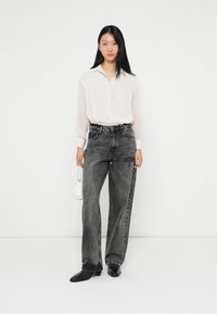Wide-leg, high-waisted black jeans with faded texture, paired with a light pink, button-up shirt. Accessories include a small white handbag.