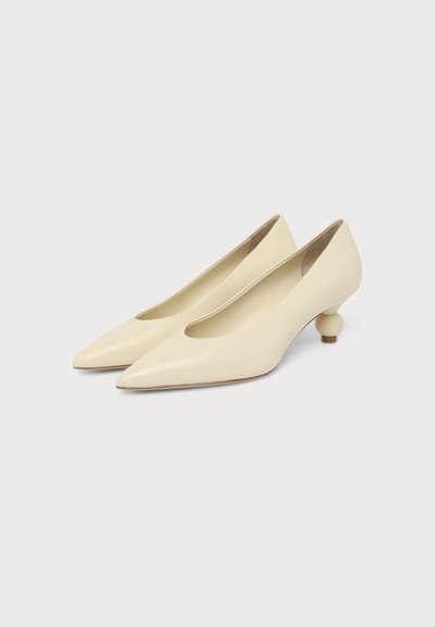 Escarpins bas couleur crème pour femmes, à bout pointu avec des talons sculptés ronds uniques sur un fond uni clair.