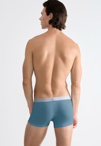 Boxer aderenti blu con un elastico grigio chiaro in vita, caratterizzati da una texture liscia e un design aderente, visti da dietro.