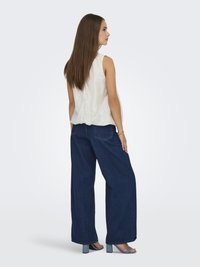 Un top sans manches blanc avec une coupe décontractée, associé à un jean en denim bleu à jambes larges, comportant deux poches arrière et des sandales à talons bleu clair.