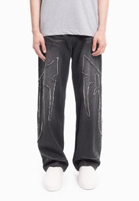 Czarne dżinsy z denimu z przetartym białym przeszyciem w kształcie błyskawicy, luźnym krojem i widocznymi kieszeniami. W połączeniu z białym obuwiem.