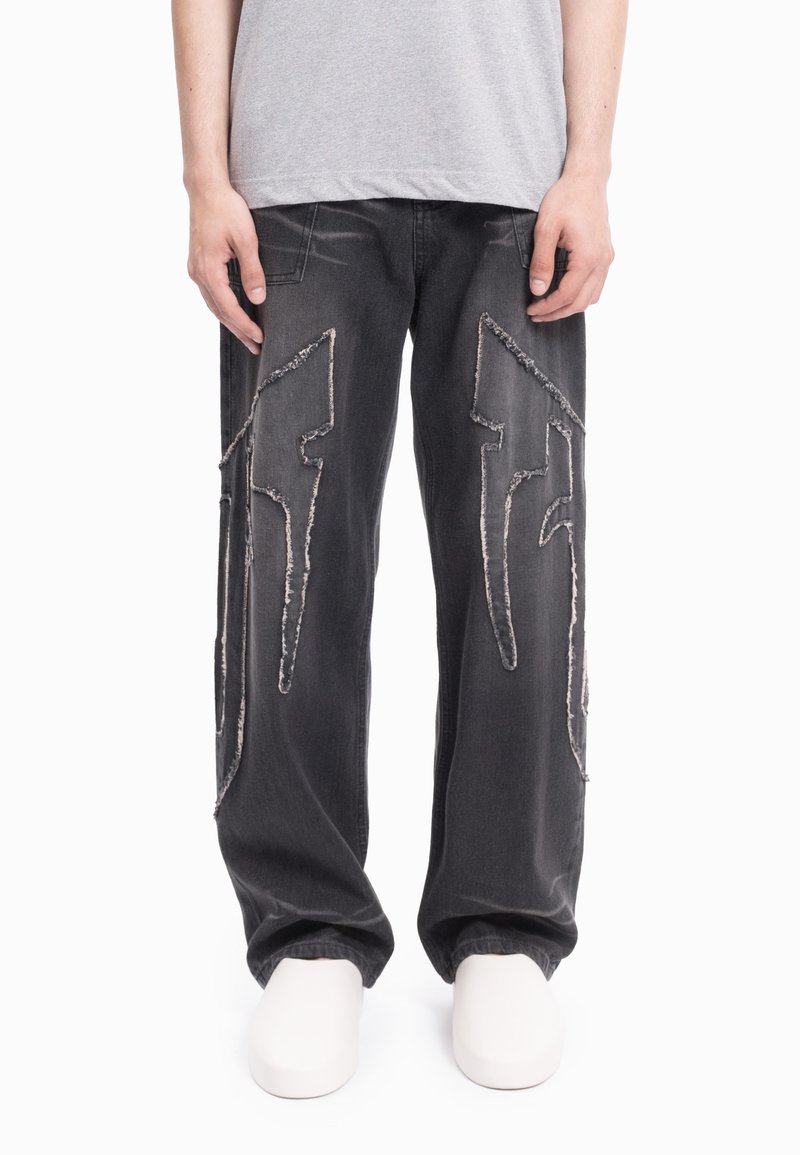 Czarne dżinsy z denimu z przetartym białym przeszyciem w kształcie błyskawicy, luźnym krojem i widocznymi kieszeniami. W połączeniu z białym obuwiem.