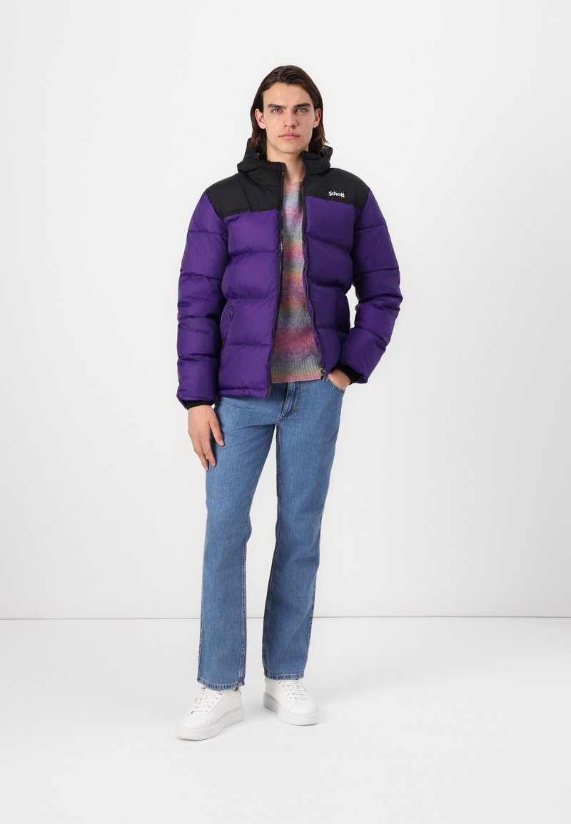 Giubbotto imbottito viola con dettagli neri, dotato di cappuccio e chiusura con zip. Indossato sopra un maglione multicolore, abbinato a jeans blu e sneakers bianche.