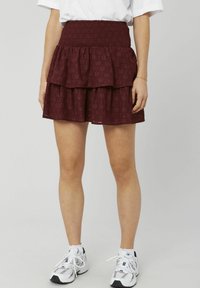 Jupe bordeaux à volants avec une taille froncée et un tissu texturé. Composée de deux couches et d'un motif circulaire. Associée à des baskets blanches.