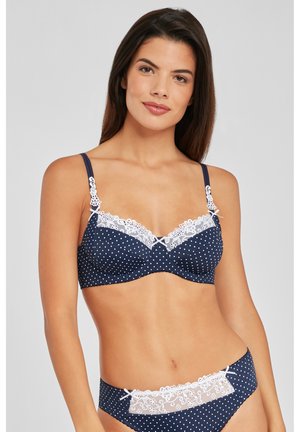 Navy-blaues Polka-Dot-BH und passender Slip mit weißen Spitzenverzierungen und dekorativen Schleifen. Glattes Material mit dezentem Glanz, vollflächiges Design.